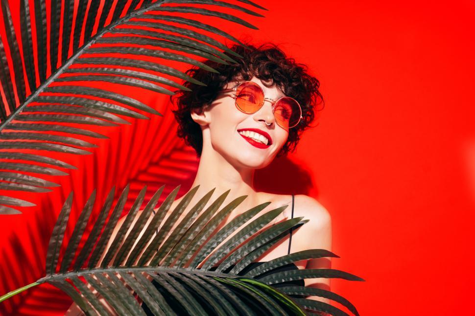 Free Image of Happy woman with sunglasses and green leaves, red background 