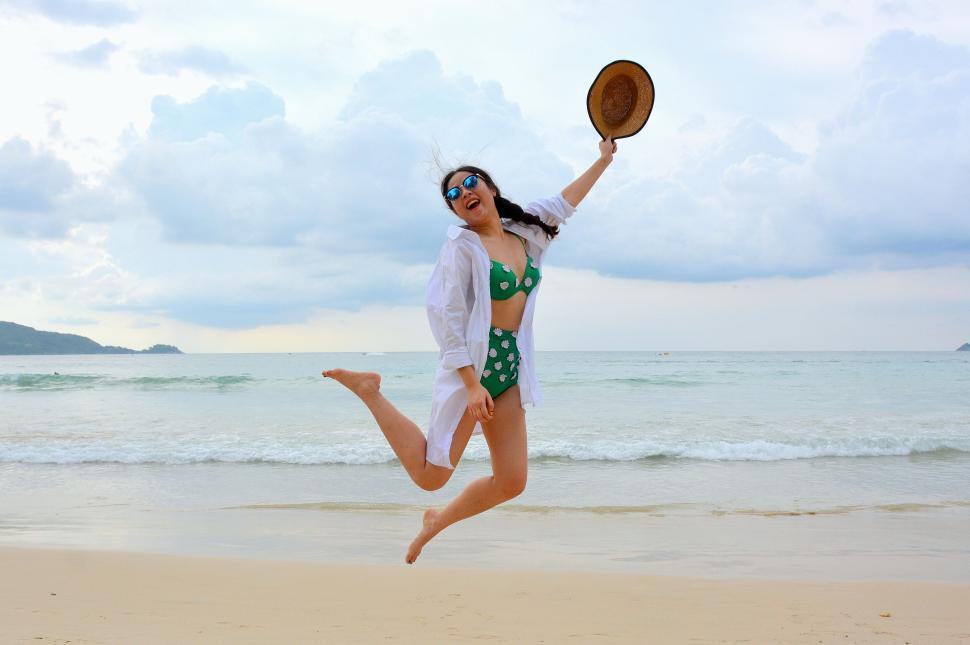 Free Image of Woman in green bikini jumping joyously on the beach 