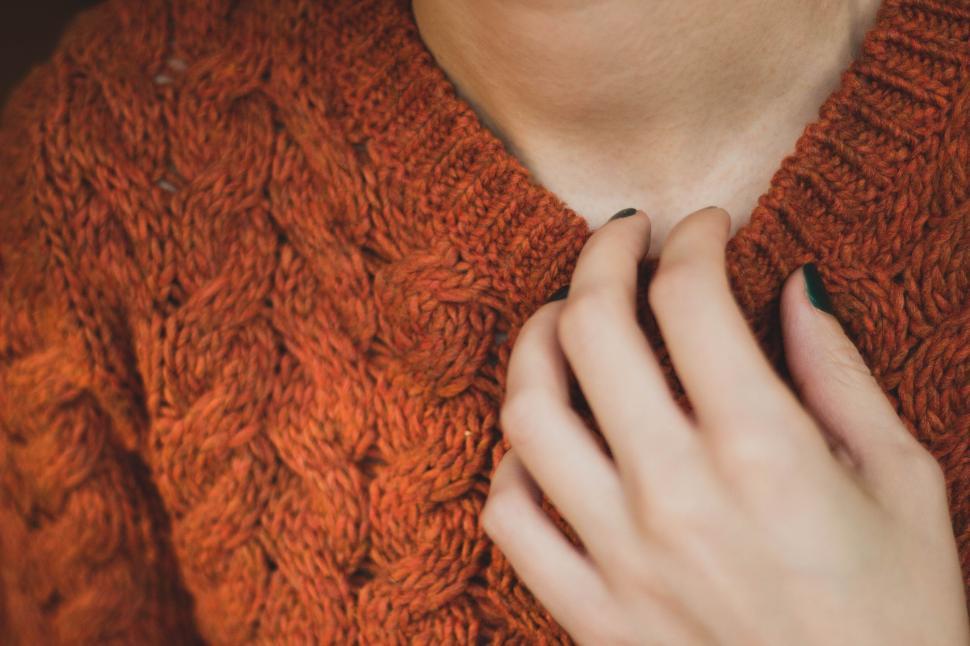 Free Image of Hand on an orange cable-knit sweater in soft focus. 