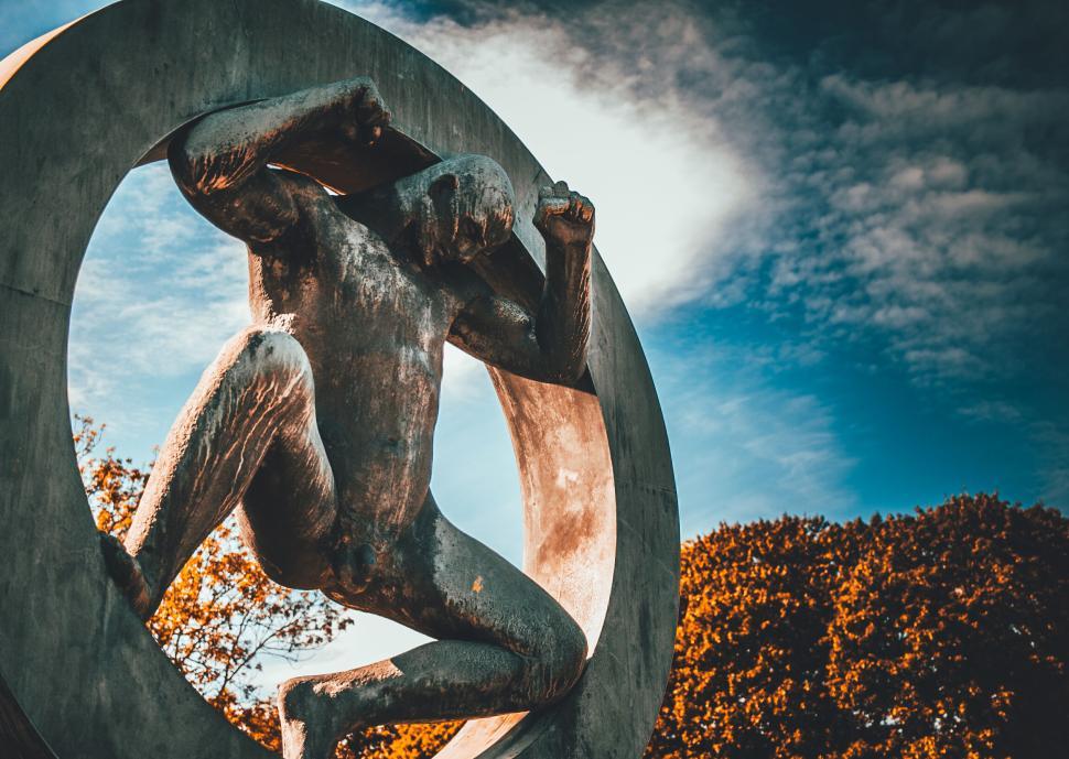Free Image of Statue of a man pushing against a circular frame. 