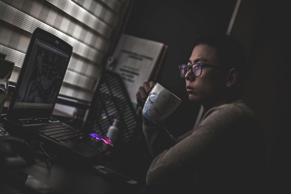 Free Image of Person drinking coffee while working on laptop at night 
