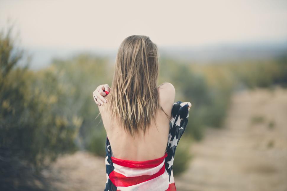 Free Image of Woman wrapped in American flag facing wilderness behind. 