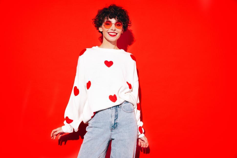 Free Image of Cheerful woman with big red hearts sweater, red background 