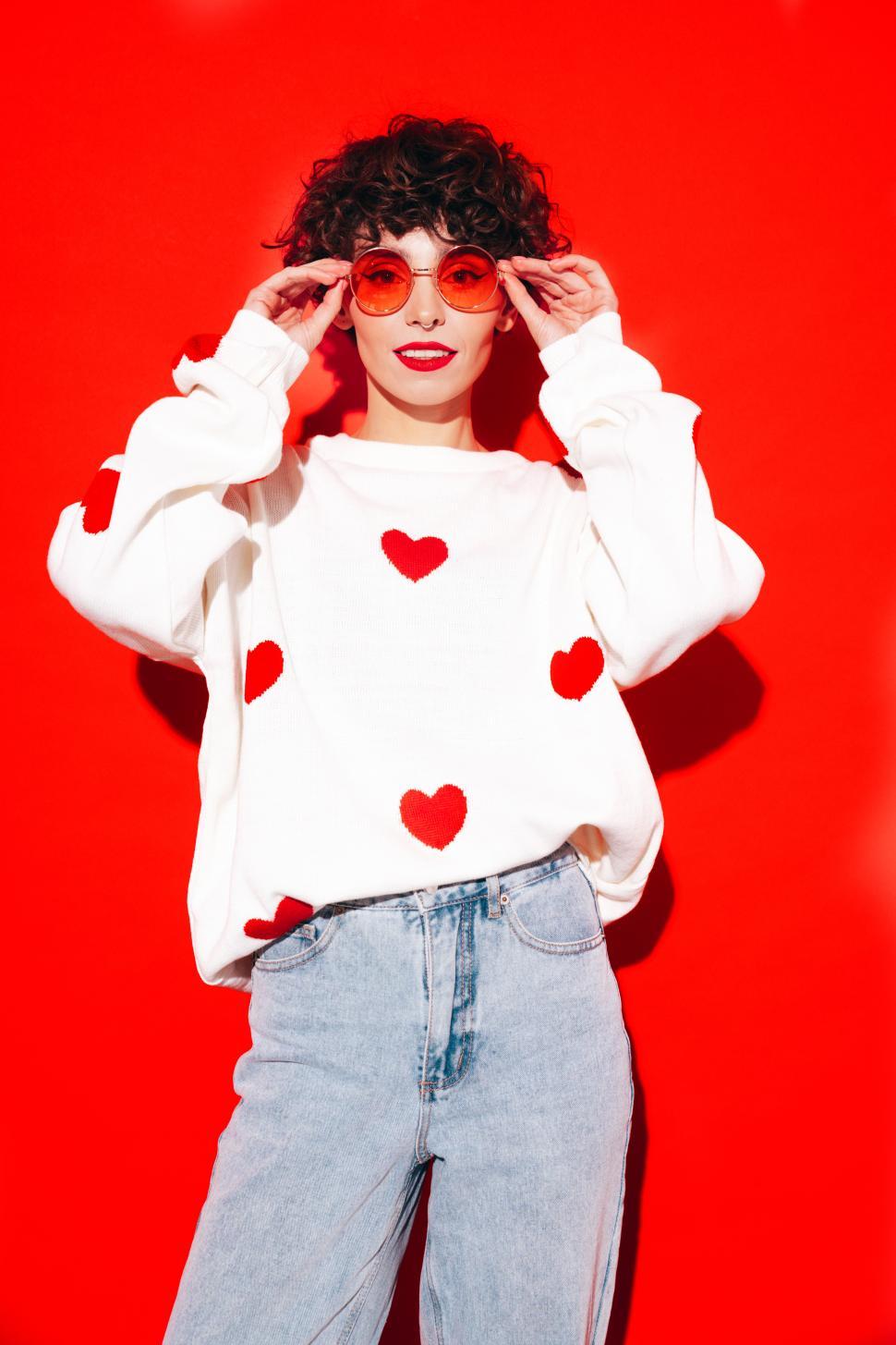 Free Image of Chic woman adjusting sunglasses, heart-patterned sweater on 