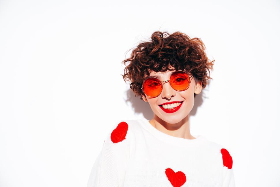 Free Image of Cheerful woman with orange glasses smiling, heart sweater on 
