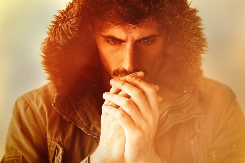 Free Image of Pensive man in fur-lined jacket with hands together 