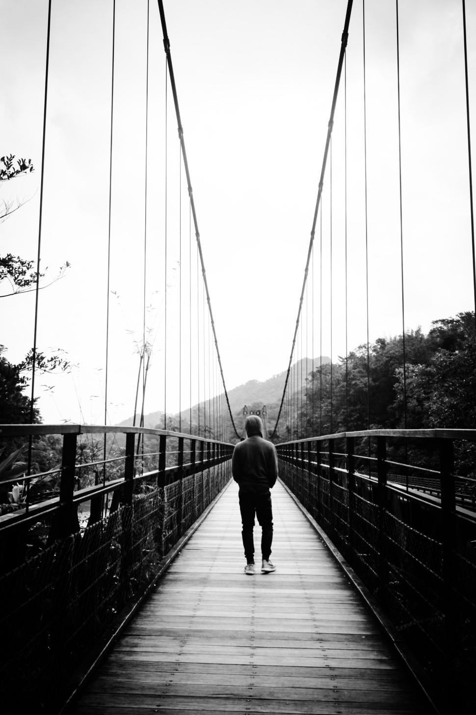 Free Image of Man walking alone on a suspension bridge in monochrome 