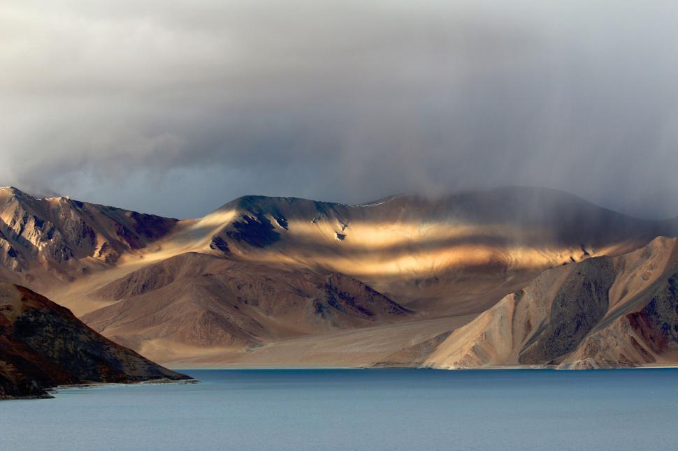Free Image of Sunlit mountain ranges with a serene blue lake beneath 