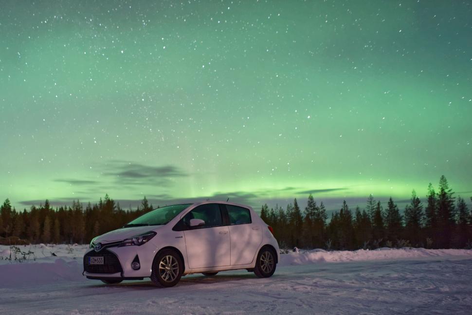 Free Image of White car parked under northern lights in snowy landscape 