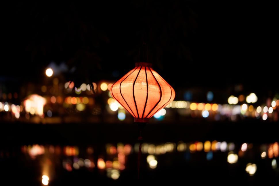 Free Image of Lit lantern hanging in night with blurred lights behind 