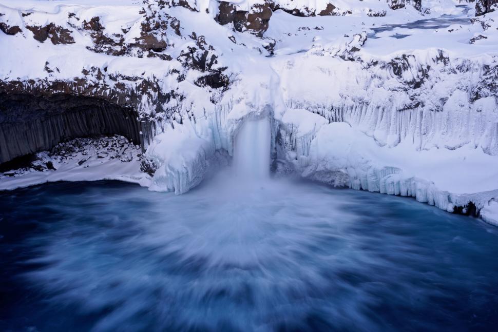 Free Image of Frozen waterfall amidst snowy cliffs and calm water 