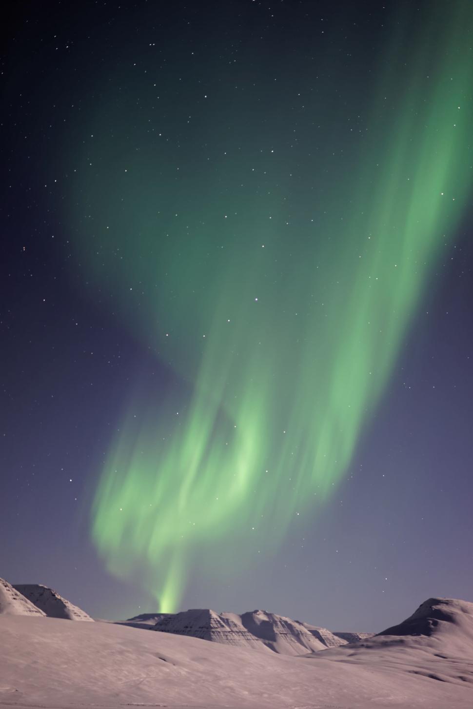 Free Image of Northern lights spiral down over snowy mountains 