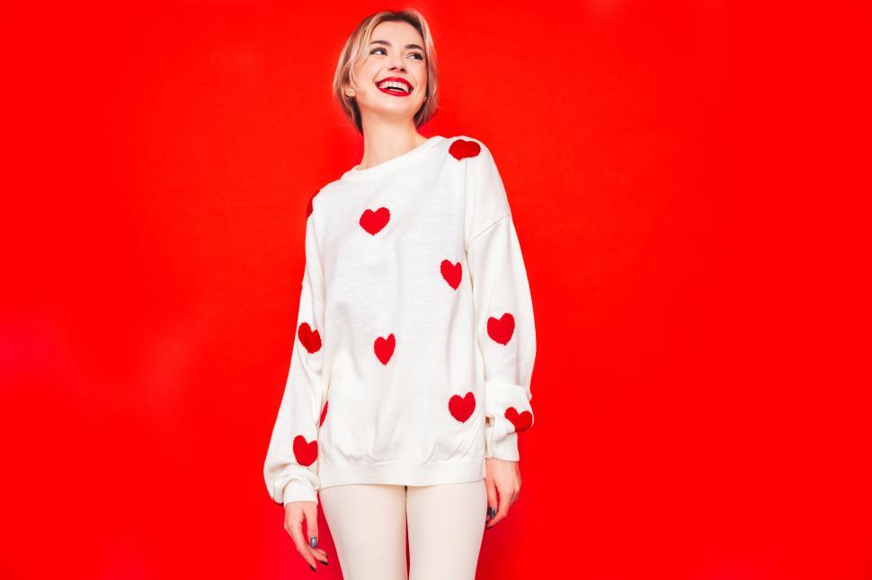 Free Image of Woman posing in white sweater with red heart patterns 