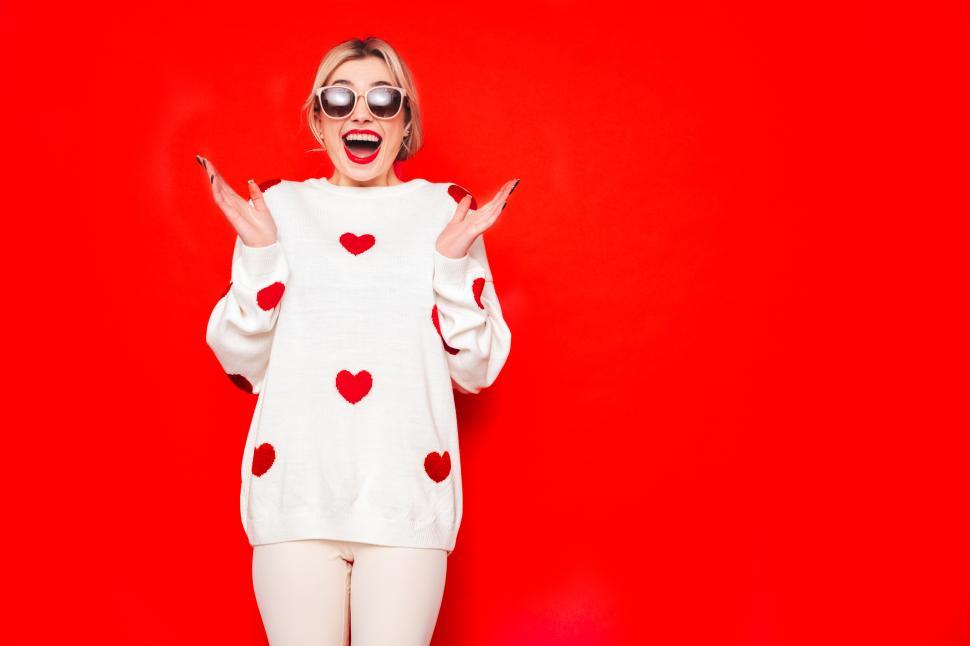 Free Image of Woman in white sweater with red hearts, red background. 