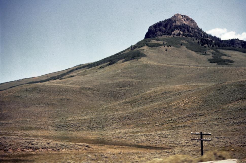 Free Image of Mountain peak rises above a grassy, sloping landscape. 