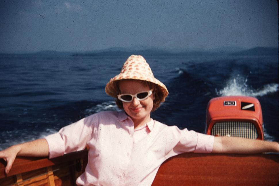 Free Image of Woman on a boat wearing hat and sunglasses, smiling. 