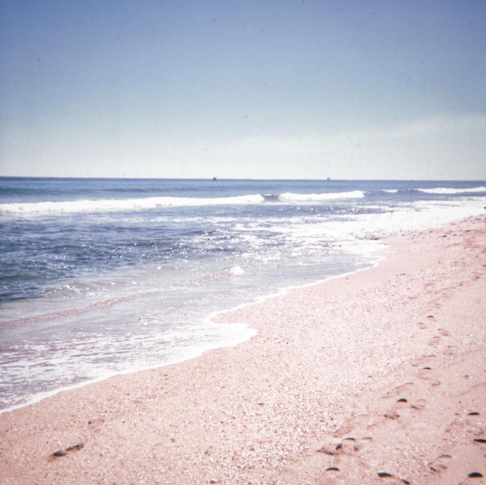 Free Image of Pink sandy beach with waves and blue ocean, clear sky. 
