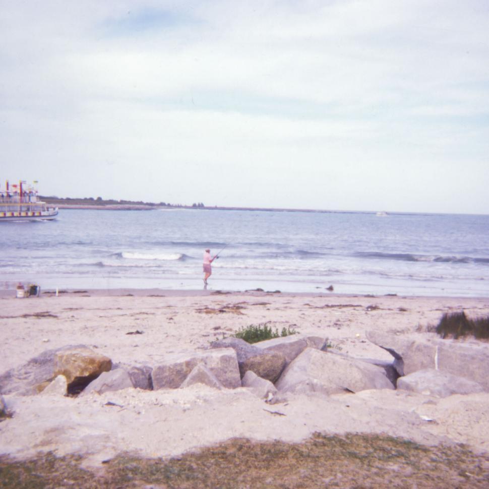 Free Image of Fishing on sandy beach with rocks and distant boat views. 