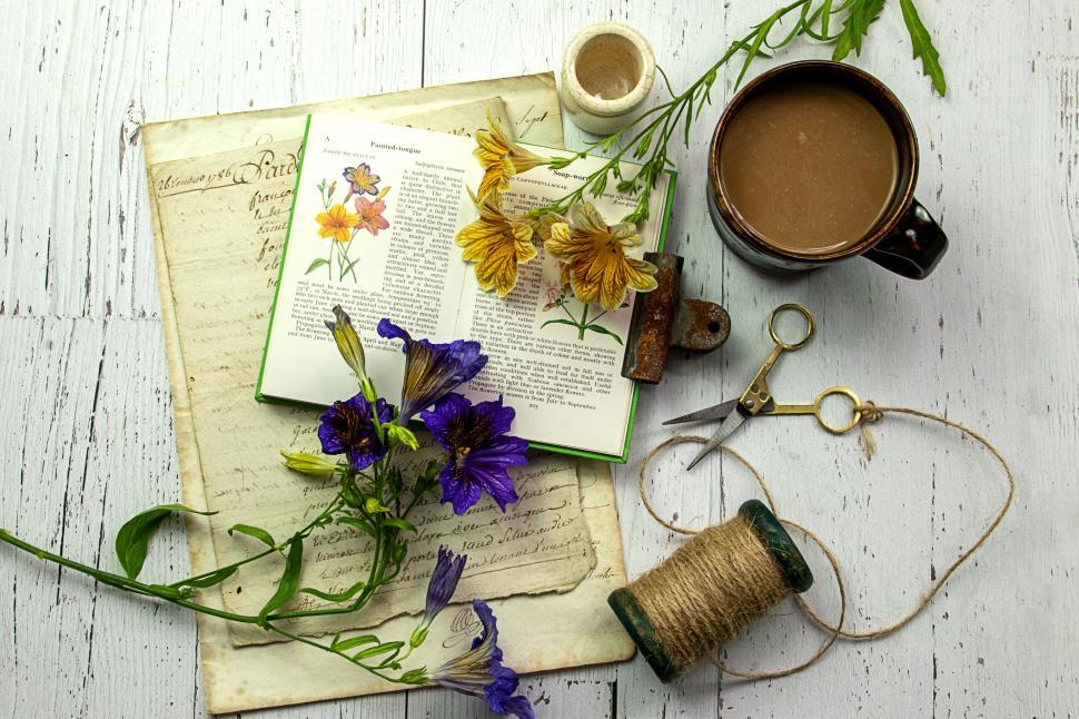 Free Image of Book and flowers on a desk with coffee cup and tools. 