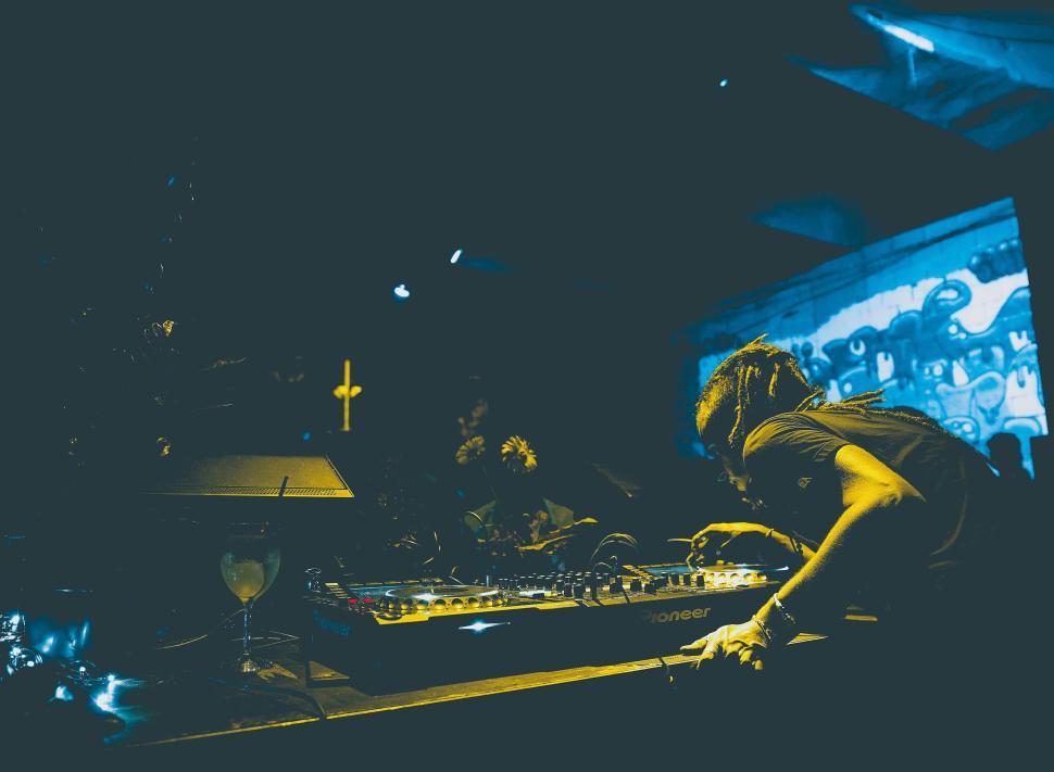 Free Image of Busy DJ working at a sound mixer in a dark club scene. 
