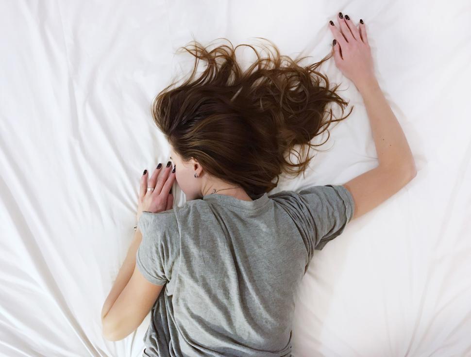 Free Image of A person lying face down on a bed with white sheets. 