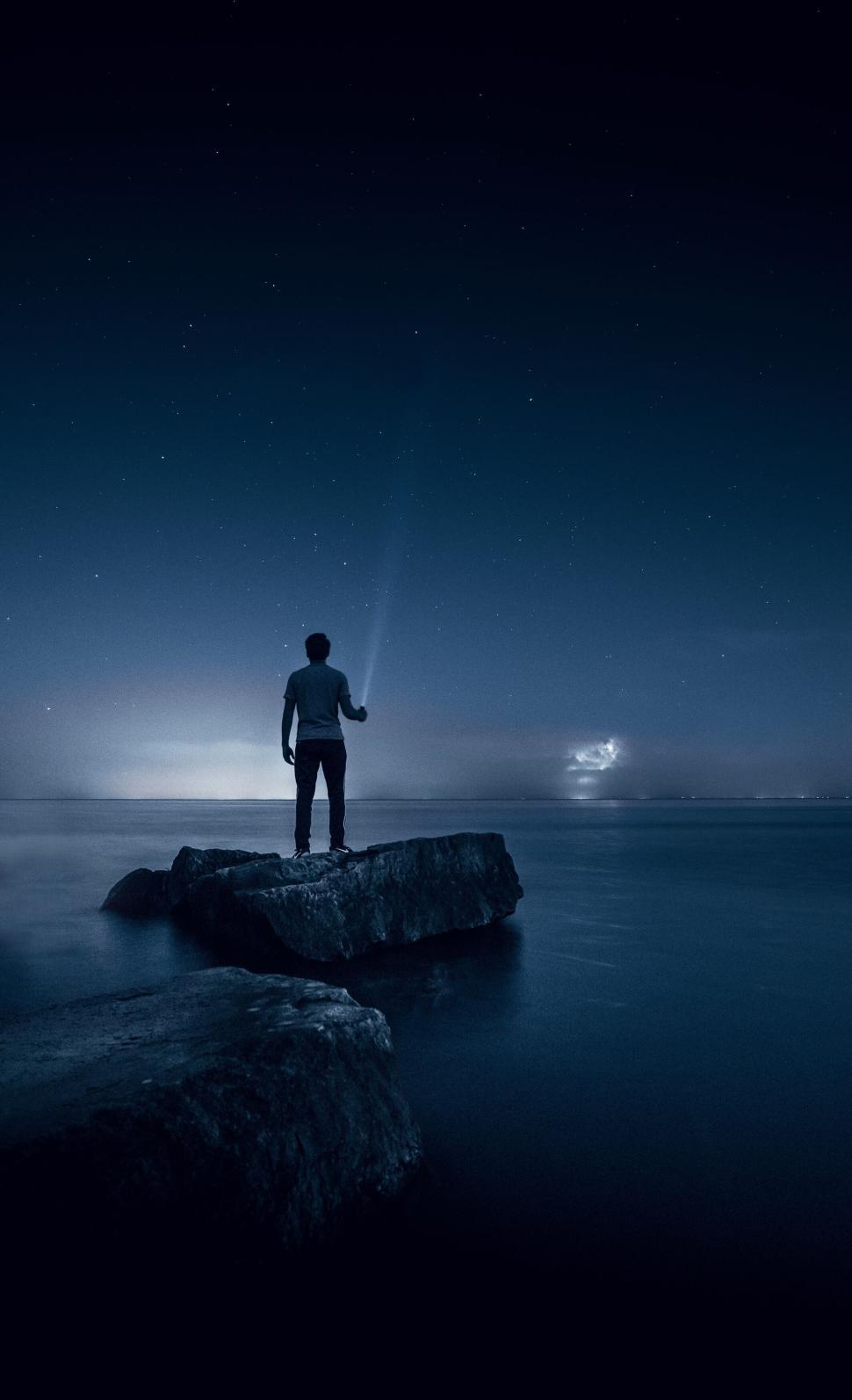 Free Image of Person standing on rocks by a tranquil night sea. 