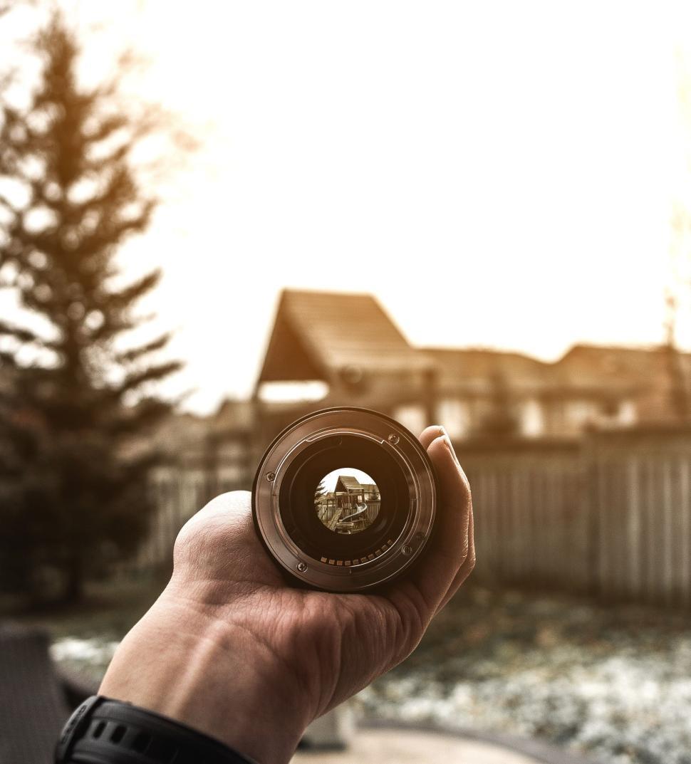 Free Image of Hand holding up a camera lens in a backyard setting. 