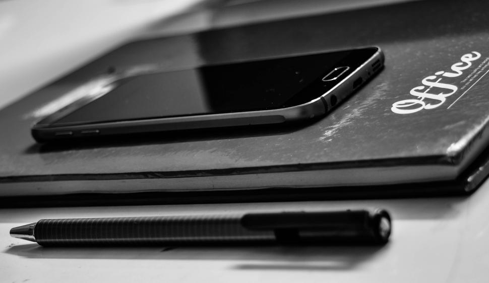 Free Image of Smartphone on notebook with pen, black and white. 