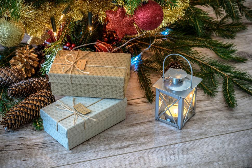Free Image of Festive Christmas presents and candle-lit lantern under tree. 