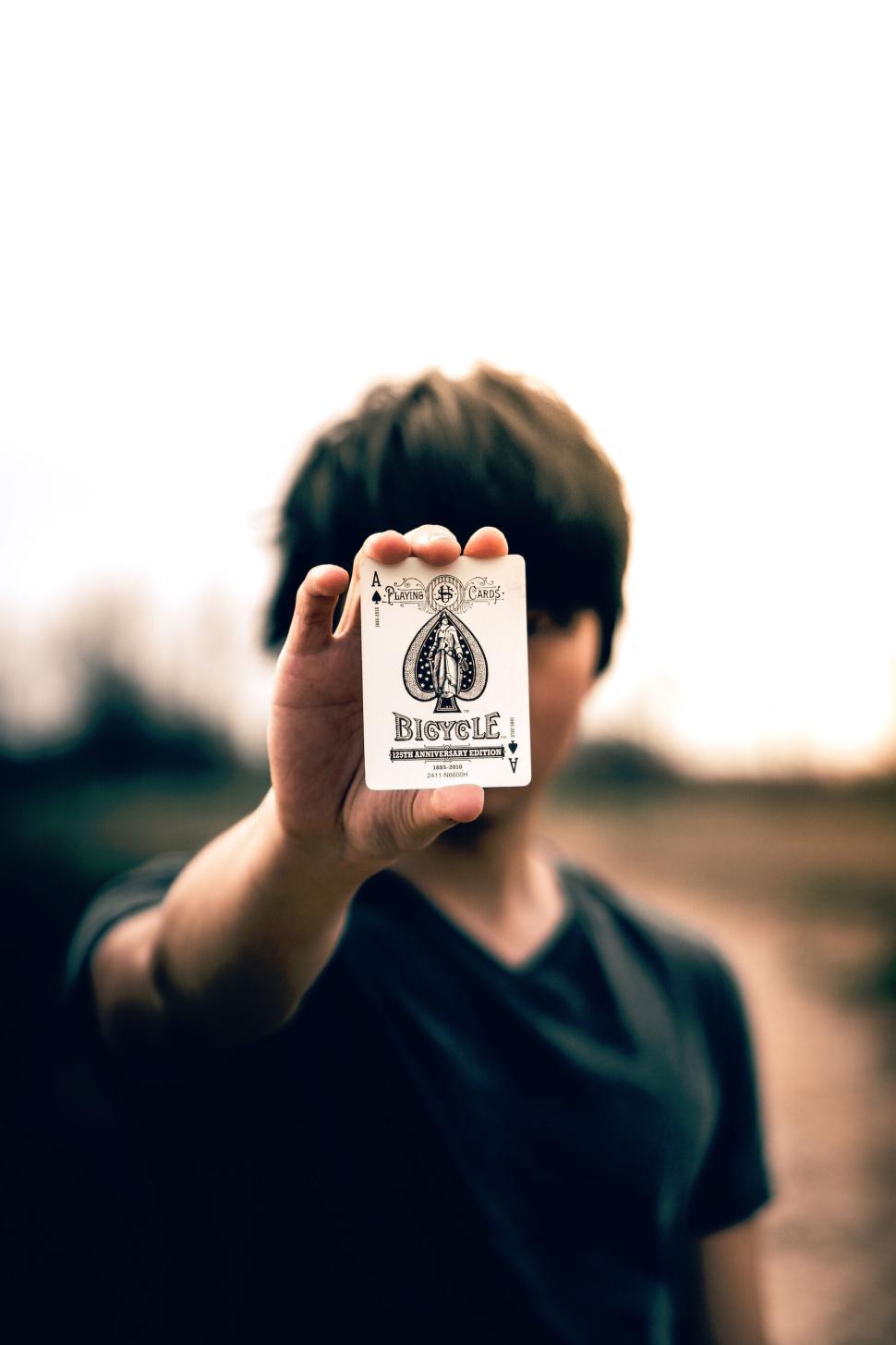 Free Image of Man holding Ace of Spades card out of focus in hand. 
