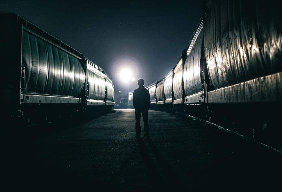 Free Image of Silhouette of person standing between two freight trains. 