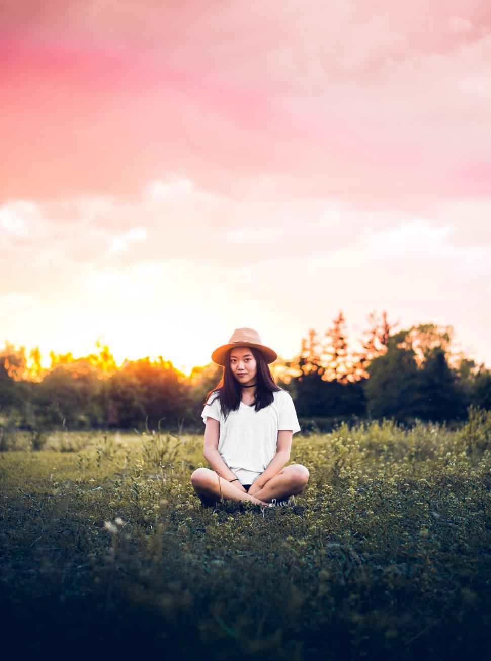 Free Image of Young woman sitting cross-legged in a field at sunset 