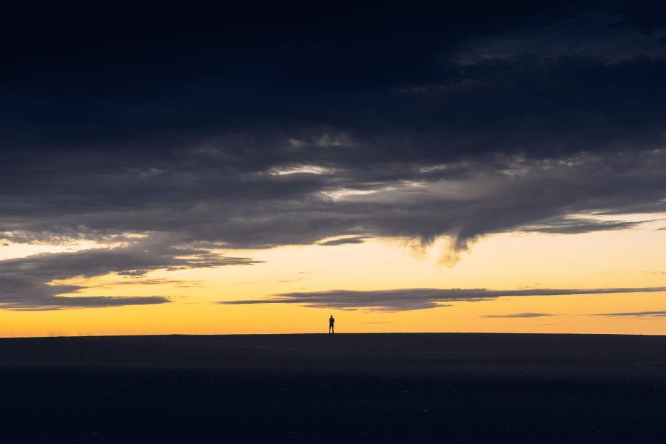 Free Image of Solitary figure standing on horizon under dramatic sky 