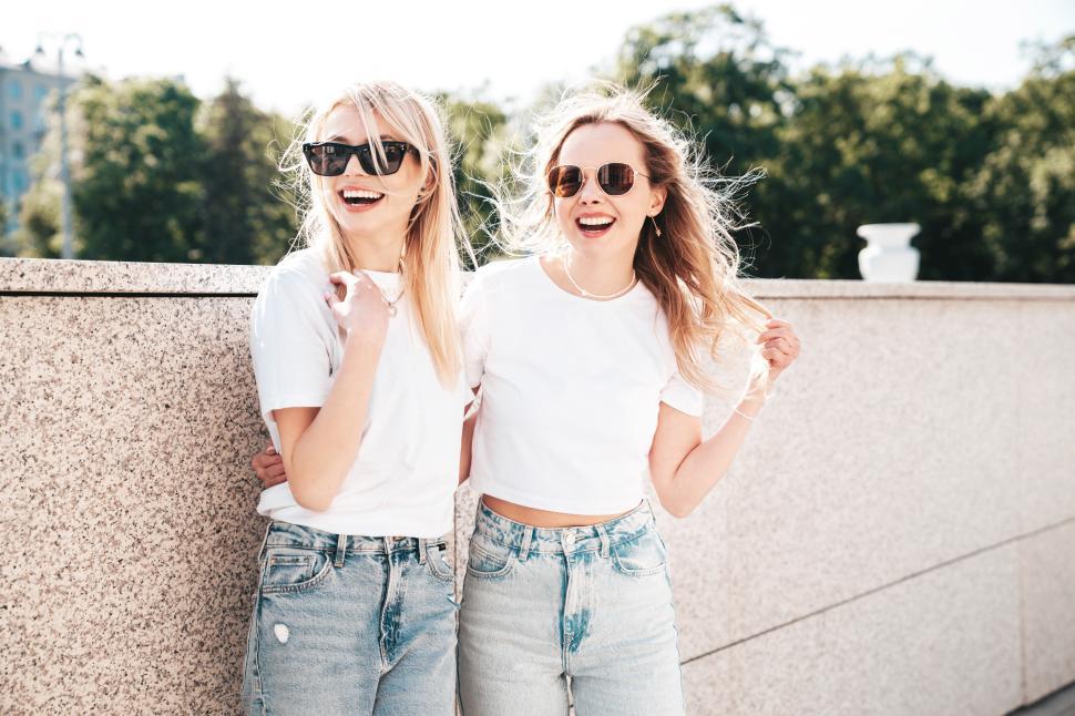 Free Image of Two cheerful young women in white shirts and sunglasses, one with arm around the other 
