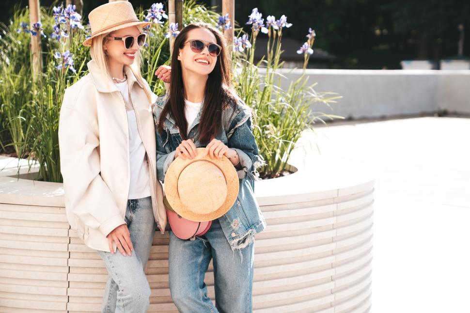 Free Image of Two stylish young women pose by a planter full of flowers 