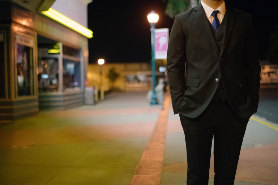 Free Image of Man in a suit standing alone on a night sidewalk 