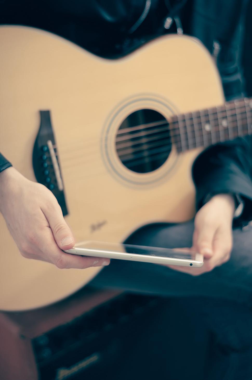 Free Image of Person holding a tablet while playing an acoustic guitar 