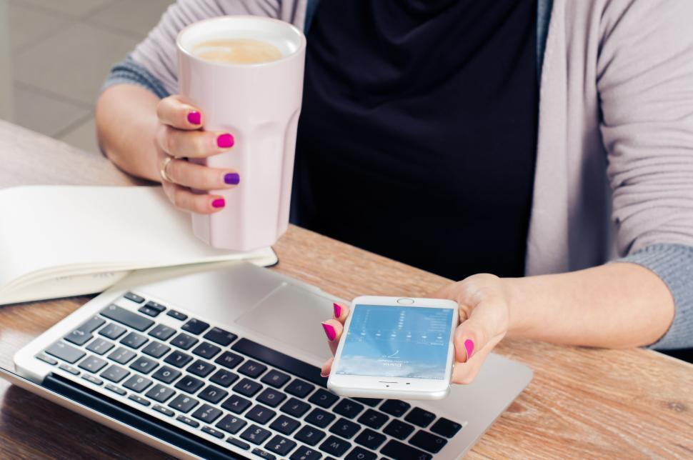 Free Image of Person with smartphone and coffee next to laptop. 