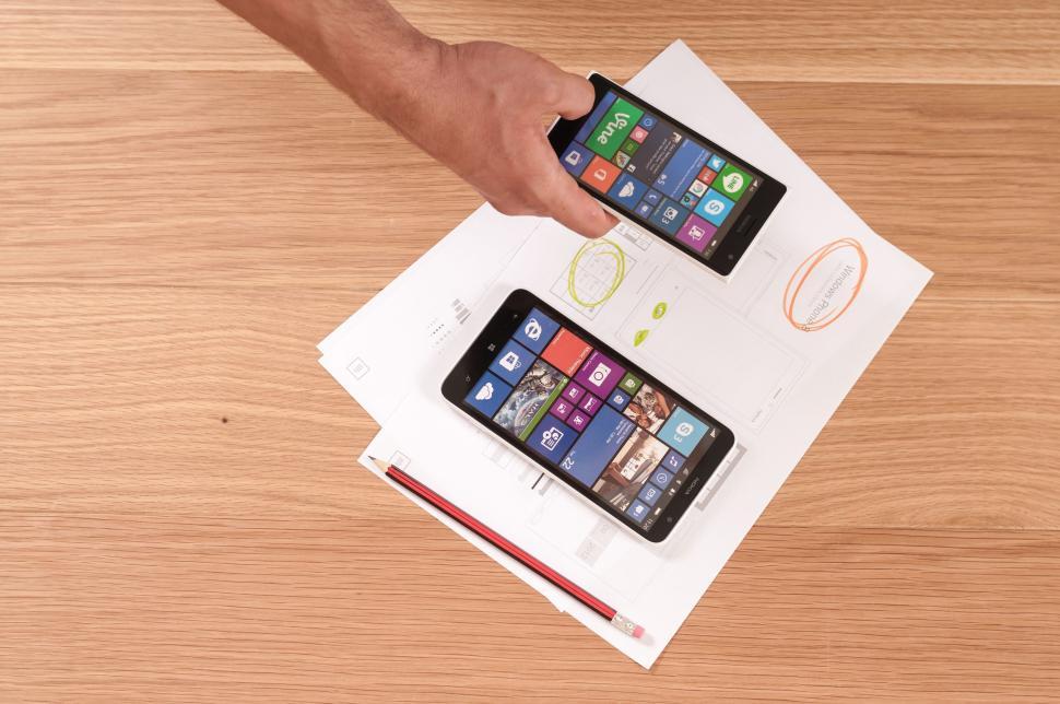 Free Image of Hand holding dual smartphones over technical drawings. 