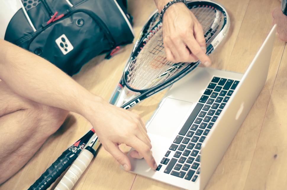 Free Image of Person using laptop with tennis racquets nearby. 