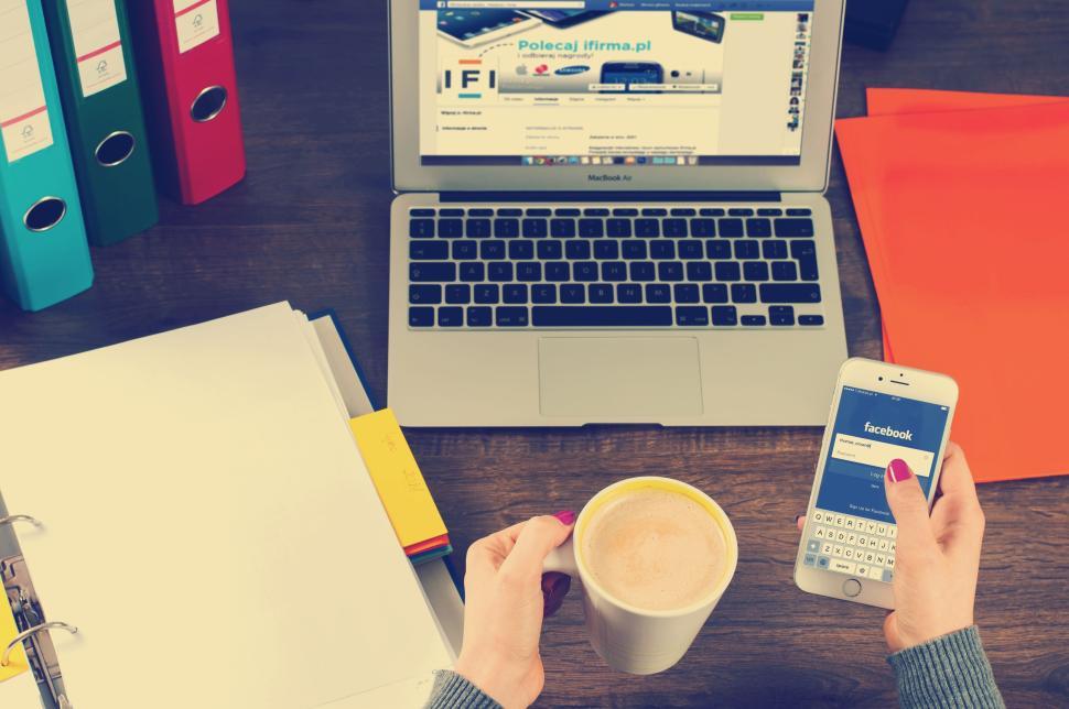 Free Image of Hand holding smartphone with laptop, coffee cup on desk. 