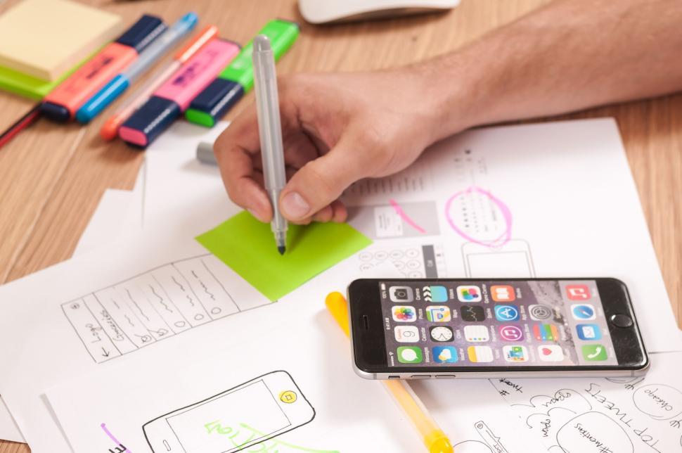 Free Image of Man writing on a sticky note surrounded by office supplies. 