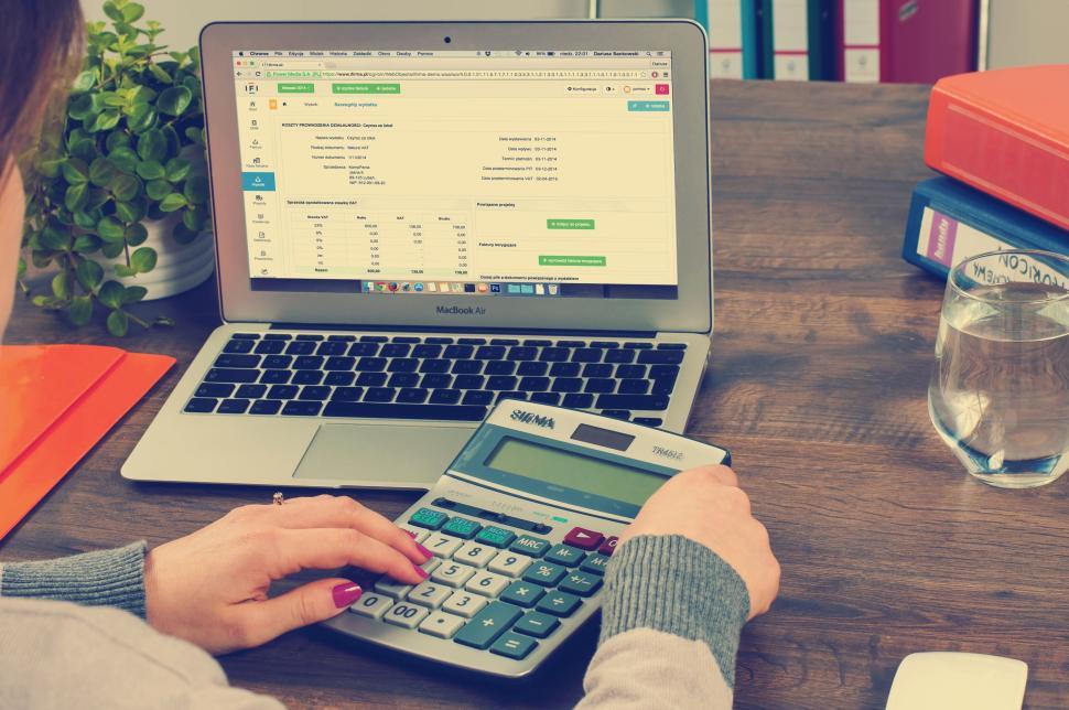 Free Image of Person using calculator with financial software open on laptop. 