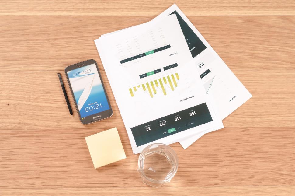 Free Image of Smartphone, papers, and a glass of water on a wooden desk. 