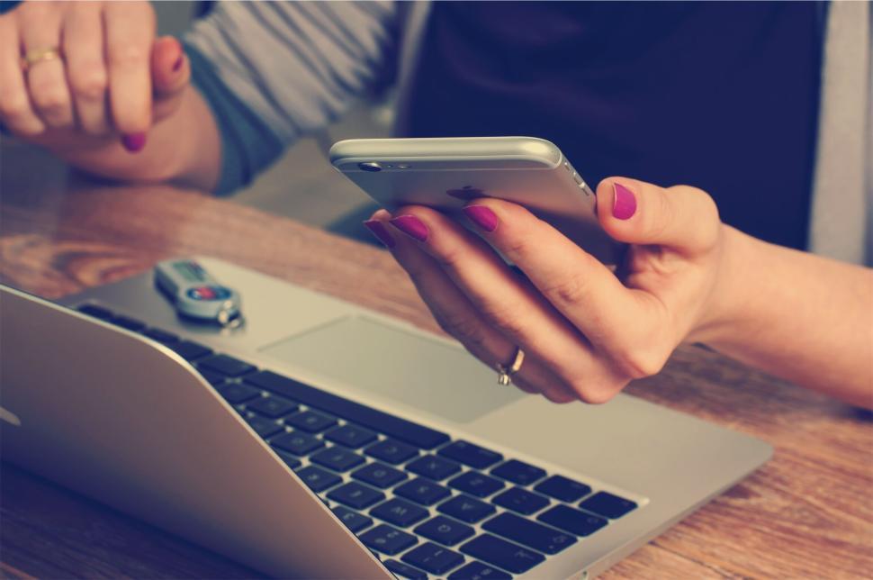 Free Image of Person holding a smartphone and working on a laptop. 