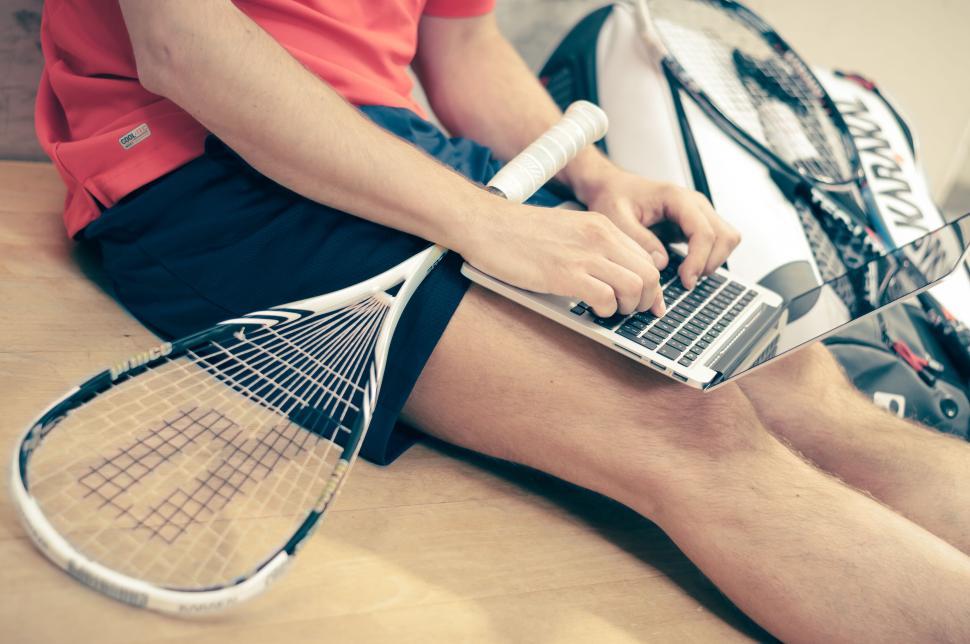 Free Image of Person with laptop and squash racket in casual attire 