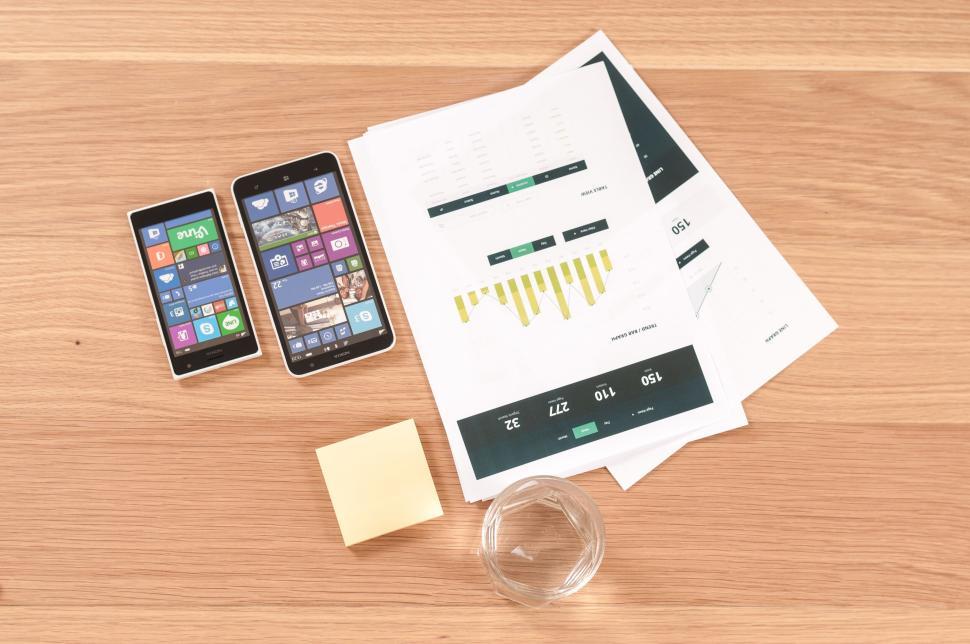 Free Image of Two smartphones with charts and papers on wooden desk 