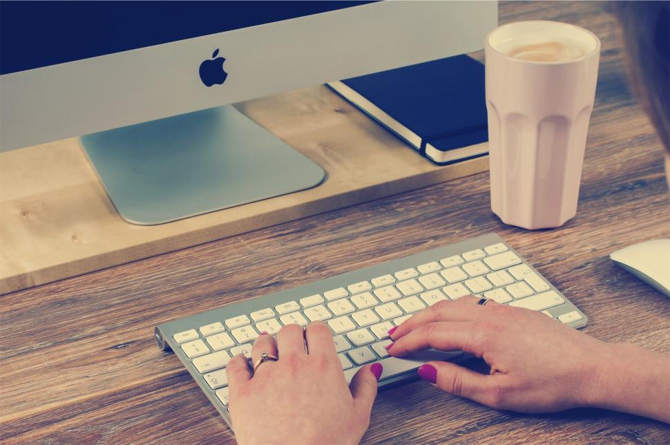 Free Image of Person typing on an Apple keyboard with a desktop in view. 