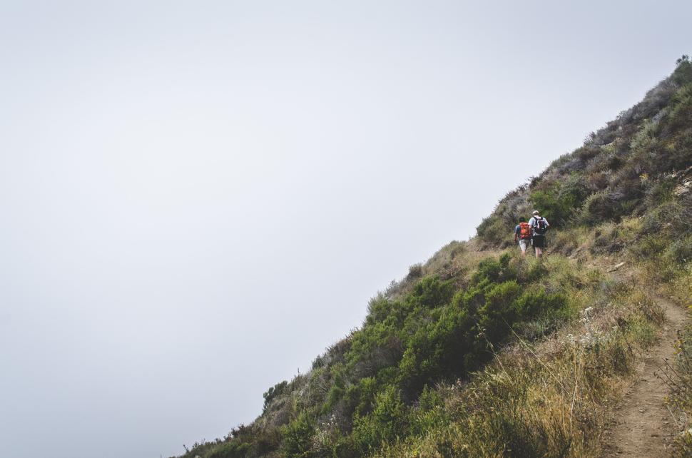 Free Image of Hikers walking on narrow hillside trail with foggy skies 