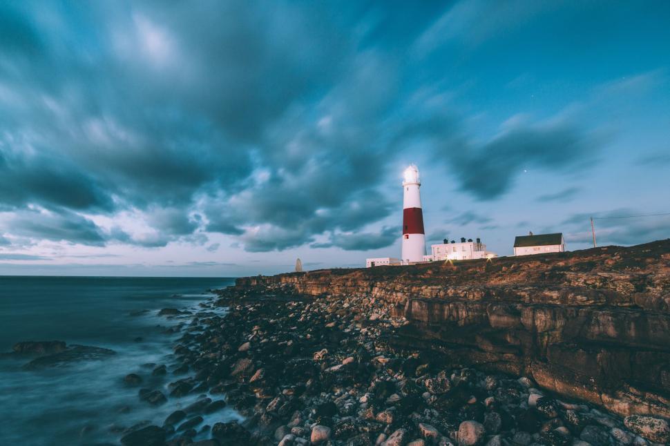 Free Image of Bright lighthouse on rocky coast with dramatic cloudscape. 